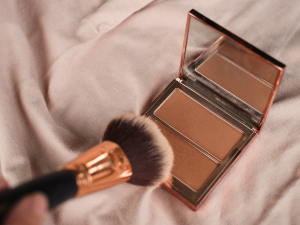 Bronzer e contorno principais diferenças. Foto embalagem de bronzer sobre a cama com lençol branco e pincel dourado.