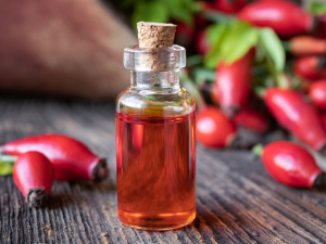 Óleo de Rosa Mosqueta. Foto mostra uma embalagem de vidro com óleo e sementes de mosqueta ao redor.