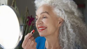mulher madura de cabelo grisalho aplicando batom